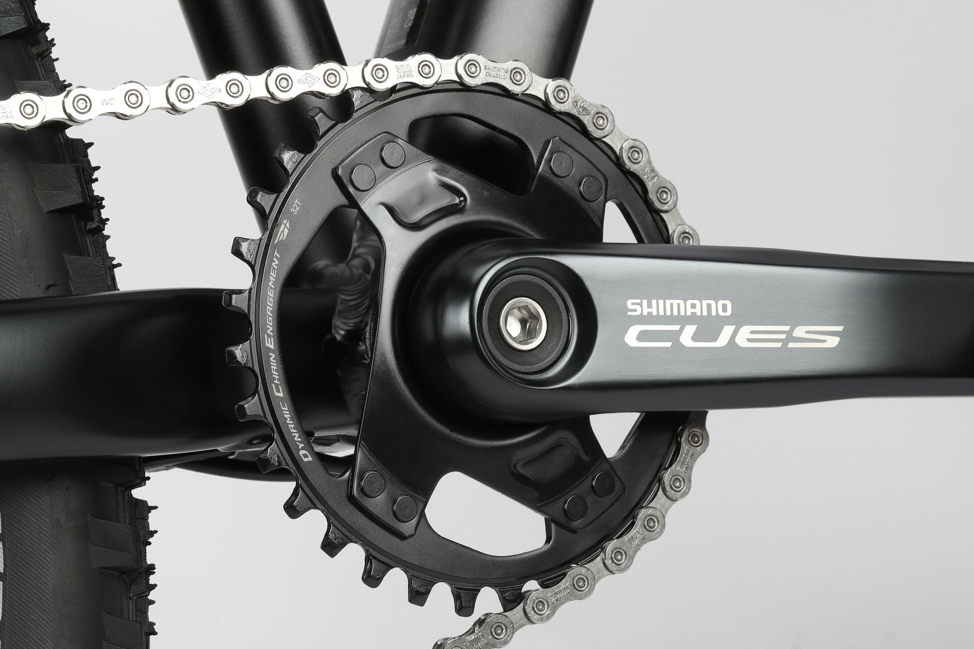 Close-up of a Double Peak 3 crankset with Shimano Cues logo, perfect for MTBs, featuring a black chainring and silver chain on gray.