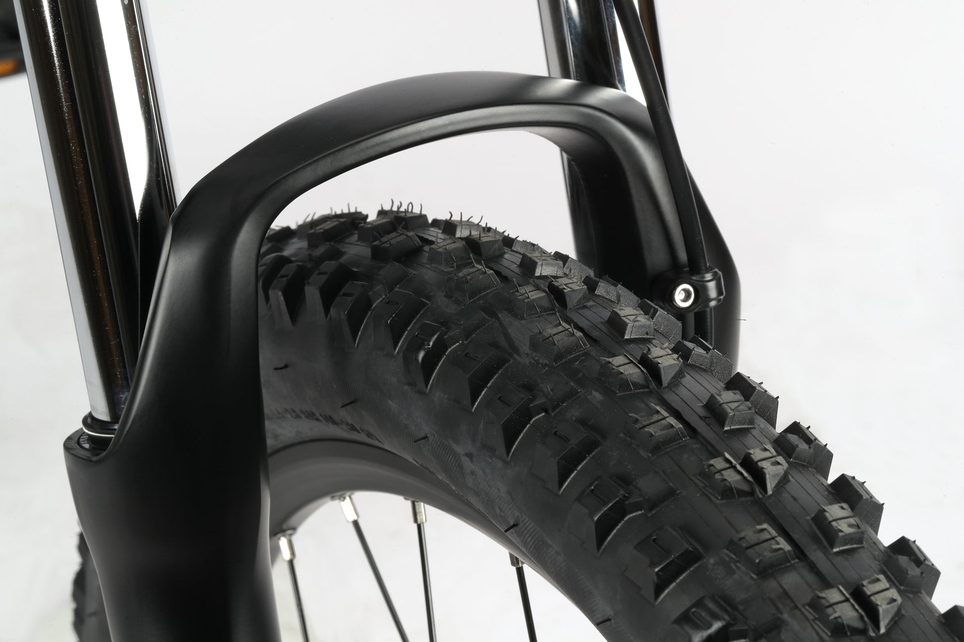 Close-up of a black tire with thick tread and suspension forks under a fender, perfect for a Double Peak 3 MTB adventure.