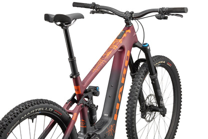 A maroon and orange eGreer Carbon 1 mountain bike with thick tires and FOX Factory suspension, viewed from the rear left.