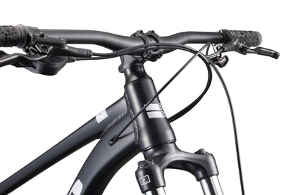 Close-up of Double Peak’s black handlebars, front suspension fork, and hydraulic disc brakes against a white background.