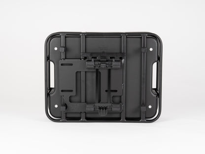 The Atran Velo Bakery Crate is a black plastic wall mount bracket with multiple slots and two side handles, designed for securing equipment. Positioned on a white background, its structure and design features are reminiscent of a cargo-style bike basket.