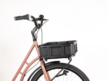 The Bakery Crate by Atran Velo showcases a brown bicycle frame with a large black cargo basket above the front wheel, complemented by a black handlebar and bell, all set against a plain white background.