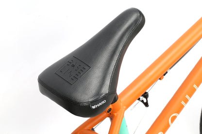 Close-up of a black bicycle seat labeled Boulevard 20.5 on an orange BMX frame from Haro Bikes. The durable, sleek seat is attached with a visible bolt, and the frame features vibrant orange, black, and aqua colors with a partial logo.