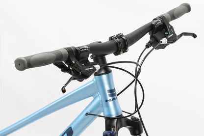 Close-up of the Bridgeport ST MicroShift handlebar and front frame from Haro MTB. It has gear shifters and brake levers with a sleek design. The light blue frame features neatly arranged visible cables, with HAW partially visible on it.