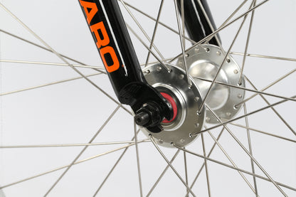 Close-up of the DMC 24 BMX wheel hub by Haro Bikes, featuring silver spokes and a black fork. An orange label is partly visible on the fork against a plain white background, highlighting its sleek design often matched with freestyler bars for ultimate agility.