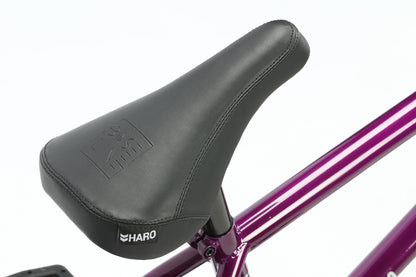 Close-up of a black Dana bicycle seat by Haro Bikes with the Haro logo against a vibrant purple frame, showcasing responsive geometry. The seat has smooth leather-like material and stitching details, while the chromoly frame stands out against a plain white background, highlighting the bikes components.