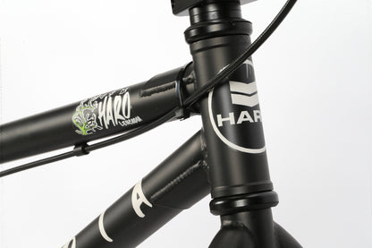 Close-up of the Leucadia from Haro Bikes with a black frame, featuring the Haro logo and graphic detail. The intricately wrapped bike cable highlights its sturdy construction and sleek design, ideal for neighborhood cruising or skatepark visits.