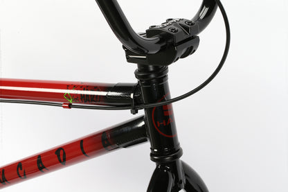 Close-up of a BMX bikes handlebars and frame. The frame is red with black accents, and the handlebars are black. A green sticker and Leucadia by Haro Bikes are visible on the frame, ready for action in your neighborhood, set against a plain white background.