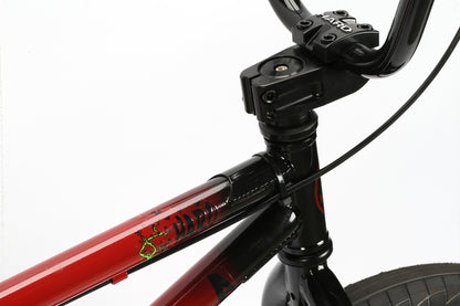 Close-up of a Leucadia BMX bike from Haro Bikes at the skatepark. The red and black handlebars and frame have thin brake cables and a sturdy metal stem. The frame features a stylized logo on the top tube, making it perfect for shredding through the neighborhood.