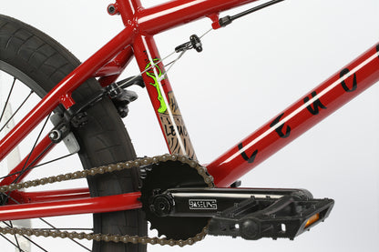 The Haro Bikes Leucadia BMX bike features a red frame with black pedals and chain, bold black text, and a neon green design. The bikes braking and chain mechanisms stand out against a white background, ready to glide through the neighborhood skatepark.