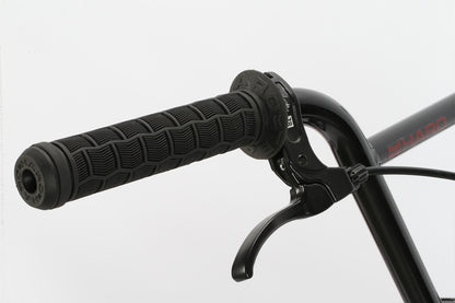 Close-up of Leucadia by Haro Bikes: a black handlebar with textured grip and brake lever, reminiscent of sleek designs seen at skateparks. The plain white background highlights the handles details.