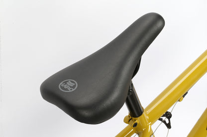 Close-up of a black bicycle seat featuring the Haro Bikes logo, mounted on a Leucadia yellow frame against a plain white background, ready to explore the neighborhood or head to the local skatepark.