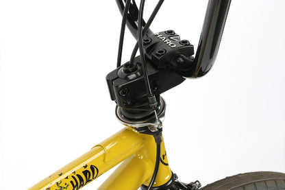 Close-up of the Leucadia DLX by Haro Bikes, showcasing a yellow frame with HARD branding on the down and top tubes. Features include a black handlebar and stem, integrated with a Gyro detangler for smooth brake cable routing.