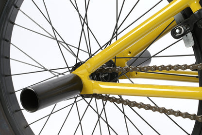 Close-up of the Leucadia DLX by Haro Bikes reveals the rear wheel and frame of this vibrant yellow freestyle BMX, highlighting detailed spokes, tire, chain, gear system, chromoly cranks, and a portion of the black metal axle peg.