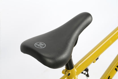 A close-up of the Leucadia DLX by Haro Bikes reveals a black bicycle seat with a logo on a yellow frame, perfect for freestyle BMX lovers. The sleek design offers style and comfort, enhanced against a plain white background that highlights its bold colors and sporty appeal.