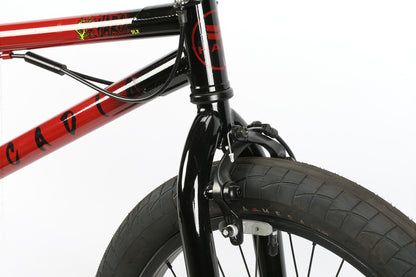 Close-up of a Haro Bikes Leucadia DLX BMX bikes front section, featuring black fork and handlebars on a red frame. The tire shows off its textured tread, with visible brake cables and a Gyro detangler, all set against a white background.