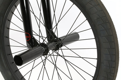 Close-up of Leucadia DLX bicycle wheel by Haro Bikes, featuring a black fork and pegs, perfect for freestyle BMX. The intertwined spokes and textured tire tread are highlighted, with focus on the lower wheel and metal axle.