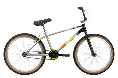 The DMC 24 by Haro Bikes features a silver and black frame with colorful accents, 24 wheels, sleek Freestyler bars, a cushioned seat, and thick tires with tan rims. Its design is modern and stylish.