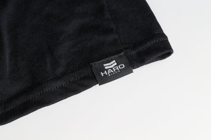 Close-up of the hem of a Haro MTB DryBlend Long Sleeve Shirt in black, featuring a sewn-in label with a white HARO Bikes logo and text. Crafted for classic fit, this shirts moisture-wicking properties enhance comfort and style.